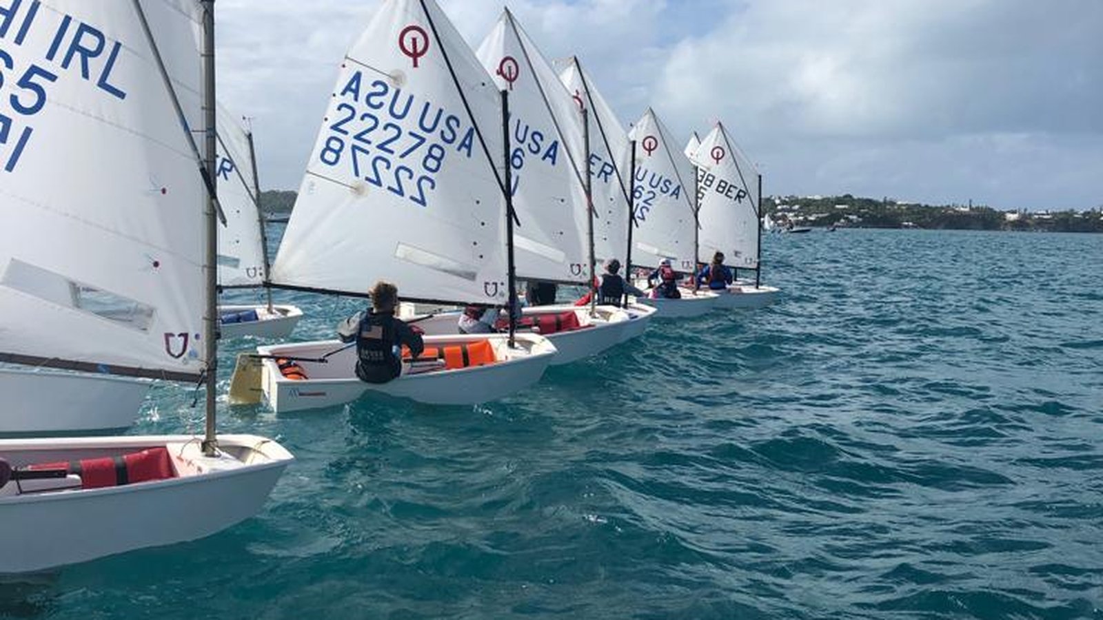 A line of Optimist dinghies sailing together